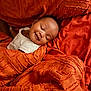 baby, sleeping, smile, blanket, orange, texture, bed, comfort, rest, peaceful, infant, face, person, young_child, cozy, soft, relaxation, indoor, cushion, cute