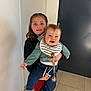 Paul participe au concours pour gagner de l'argent avec cette photo : child, baby, sibling, smile, indoor, bib, jeans, jacket, shoes, holding, freckles, portrait, happy, door, wall, tile_floor, pacifier_clip, hands, family, person