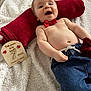 baby, infant, blanket, red_bow_tie, red_towel, milestone_card, wooden_sign, rose, jeans, bare_torso, smile, lying_down, pillow, soft_texture, fabric, portrait, indoors, cute, happy, hand