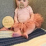 baby, infant, pacifier, headband, tutu, pink_clothing, blanket, couch, wooden_sign, two_months, sitting, cute, child, indoor, portrait, soft_lighting, young_baby, decor, foot, hand