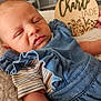 newborn, baby, sleeping, blue_outfit, striped_shirt, blanket, wooden_plaque, name_sign, indoor, closeup, infant, cute, soft_texture, resting, child, person, hand, decor, portrait, cozy