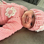 Alyzia-Mae is registered to the contest to win money with this photo: baby, infant, pink_clothing, crocheted_hat, crocheted_sweater, flower_decoration, smiling, face, headwear, lying_down, soft_surface, close_up, cute, child, portrait, indoor, warm_clothing, happy, small_person, adorable