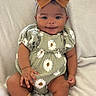 baby, child, smile, bow, headband, socks, green_outfit, daisy_pattern, sitting, blanket, indoors, cute, infant, happy, portrait, clothing, footwear, cozy, young_child, person