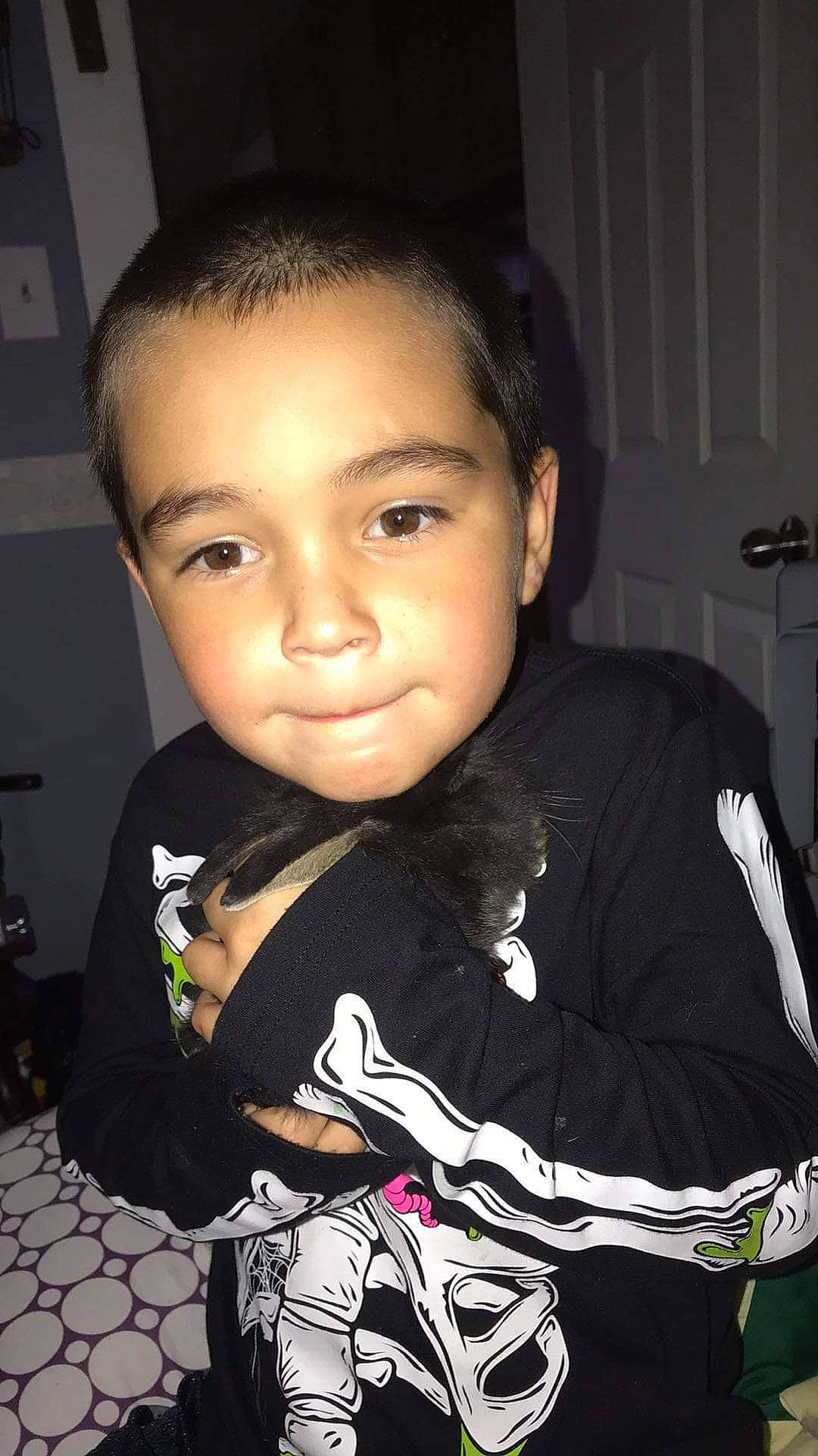 Theron is registered to the contest to win money with this photo: black, black_hair, cheek, child, chin, darkness, eyebrow, eyelash, flash_photography, forehead, formal_wear, fun, hairstyle, happy, nose, person, room, sitting, sleeve, t_shirt