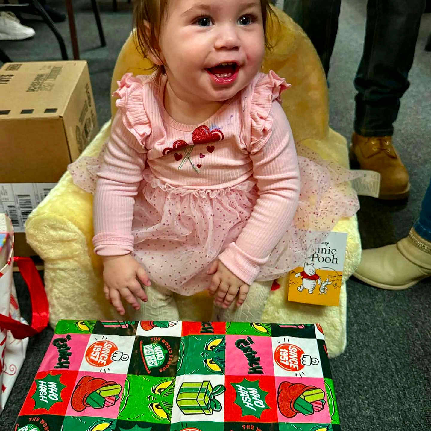 Renesmea is registered to the contest to win money with this photo: boxes, carpet, celebration, child, clothing, cute, floor, gift_wrap, happy, holiday, indoor, person, pink_dress, plush_chair, portrait, sitting, smiling, toddler, toy, winnie_the_pooh