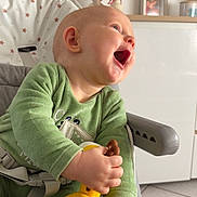 London a rejoint le concours — aidez-le/la à gagner de superbes lots ! baby, child, high_chair, toy, giraffe_toy, green_clothing, smiling, happy, indoor, home, furniture, face, hand, cute, playful, infant, seat_belt, person, portrait, toddler