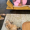 man, sleeping, tattoo, pink_shirt, yellow_couch, cat, tabby_cat, carpet, rug, living_room, slippers, wooden_table, pillow, relaxation, indoor, floor_tiles, resting, furniture, home, nap