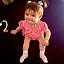 baby, child, girl, pink_clothing, pigtails, socks, smile, indoor, pacifier_clip, cushion, hair_accessories, cute, sitting, playful, face, infant, toy, floor, person, expression