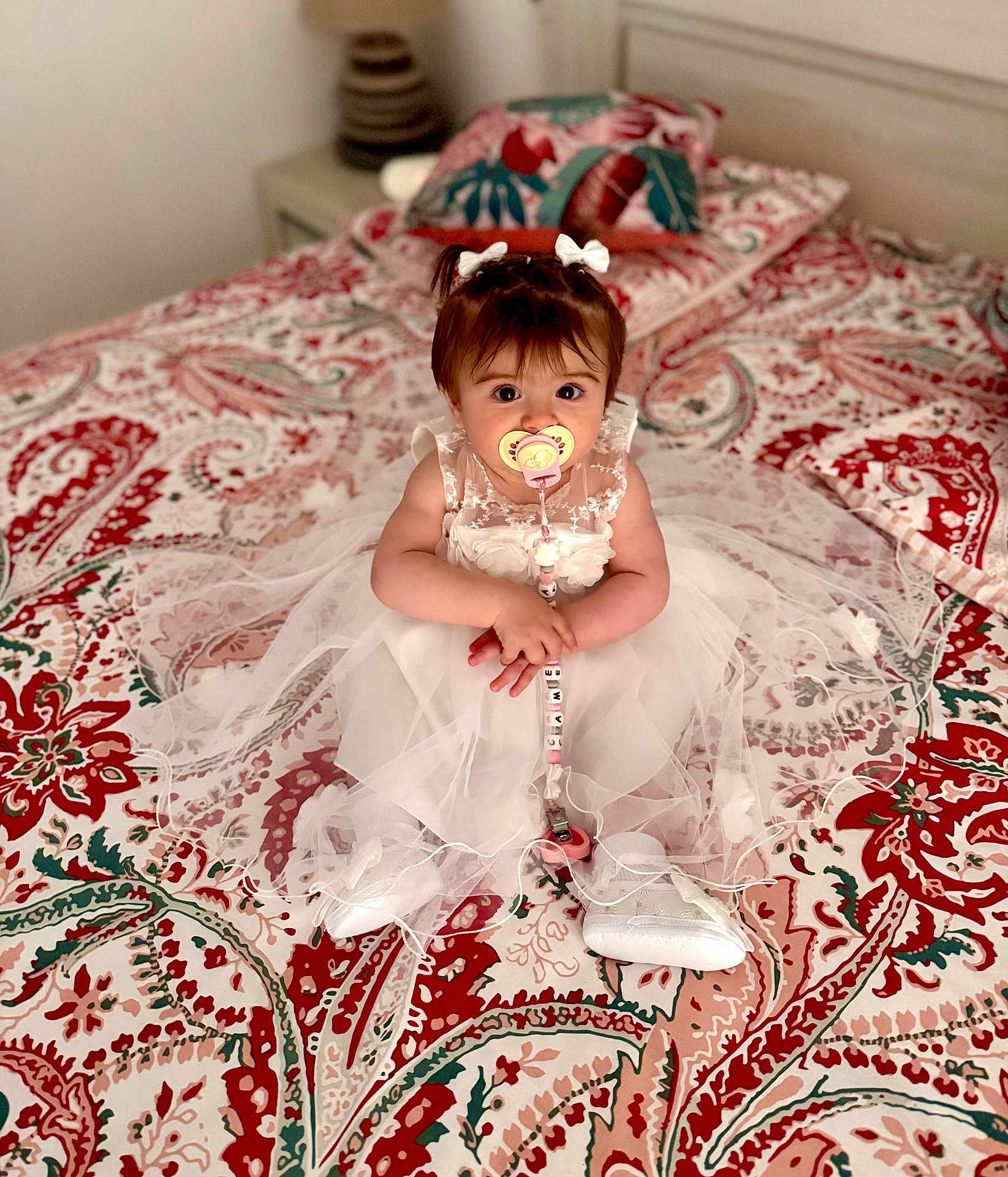 Camellia a rejoint le concours — aidez-le/la à gagner de superbes lots ! baby, child, dress, pacifier, bed, bedspread, pattern, white, pink, red, green, sitting, cute, indoors, person, footwear, hair_bows, toy, infant, portrait