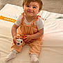 baby, child, smiling, sitting, toy, soccer_ball, orange_ball, white_socks, overalls, hair_bow, blanket, indoor, cute, playful, portrait, infant, happy, clothing, floor, person