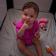 Madeleine is registered to the contest to win money with this photo: baby, blanket, child, cute, face, foot, furniture, hair, hand, indoor, infant, person, pink_clothing, playpen, plush_toy, rattle, sitting, smiling, soft_toy, toy