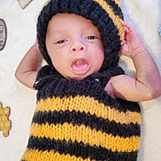 Hugo is registered to the contest to win money with this photo: baby, infant, knitted_costume, bee_costume, yellow_and_black, cute, tongue_out, soft_blanket, honeycomb_decor, handmade, cozy, newborn, portrait, laying_down, child, playful, headwear, striped, warm_clothing, adorable