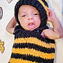 baby, infant, knitted_costume, bee_costume, yellow_and_black, cute, tongue_out, soft_blanket, honeycomb_decor, handmade, cozy, newborn, portrait, laying_down, child, playful, headwear, striped, warm_clothing, adorable