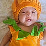 baby, infant, costume, pumpkin, orange, green, smile, face, cute, child, bedspread, pattern, soft, clothing, lying_down, happy, festive, holiday, portrait, indoors