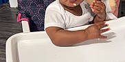 Serenity is registered to the contest to win money with this photo: baby, high_chair, food, indoor, child, face, white_clothing, flooring, toy, pink, curly_hair, person, expression, hand, foot, table, seat, real_people, infant, eating