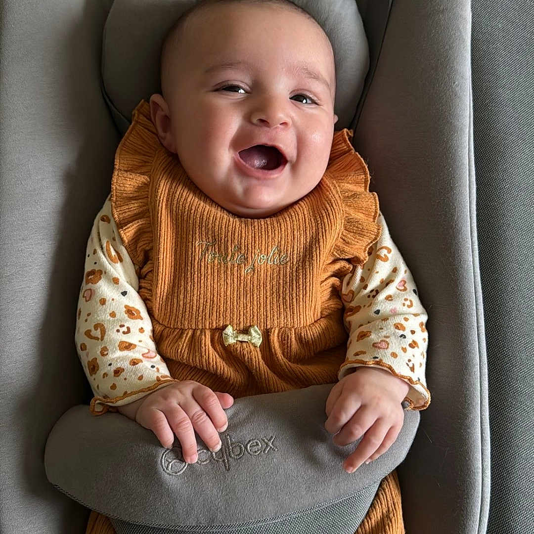 Janah a rejoint le concours — aidez-le/la à gagner de superbes lots ! baby, baby_accessory, baby_seat, child, clothing, cozy, cute, fabric, feet, footwear, hands, happy, indoors, infant, orange_clothing, portrait, seat, sitting, smiling, soft_texture