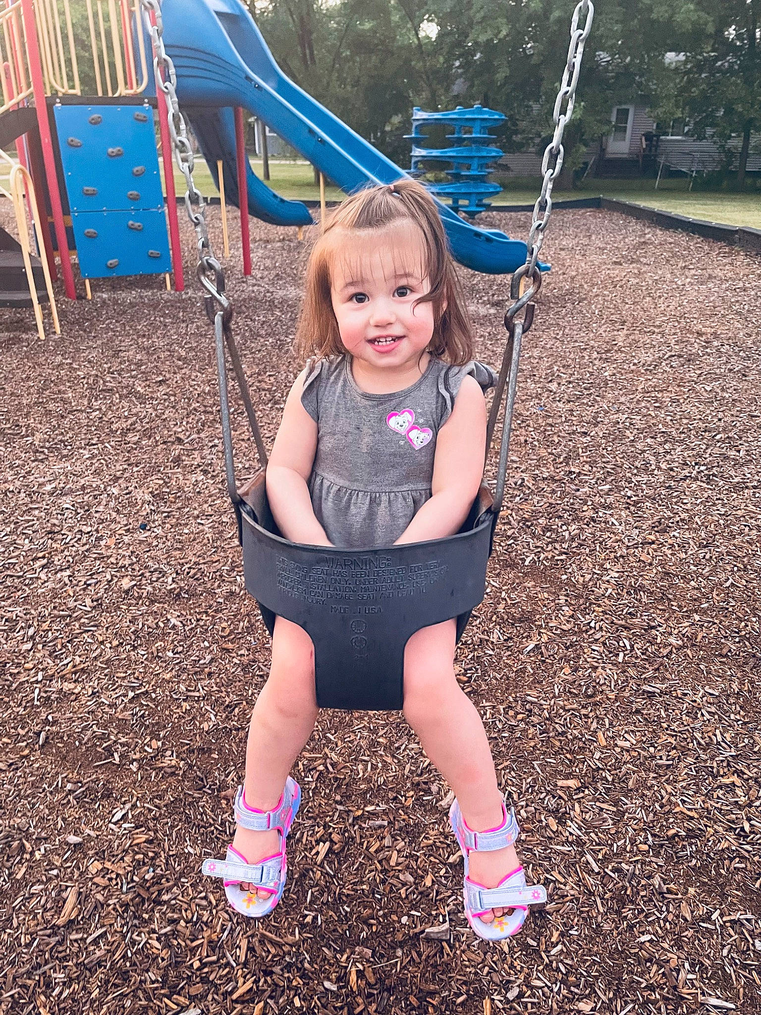 Kiara is registered to the contest to win money with this photo: child, city, eye, face, fun, grass, happy, human_body, joy, leisure, light, people_in_nature, person, photograph, plant, playground, public_space, smile, summer, swing