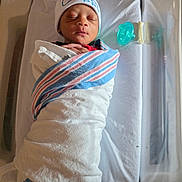Cassius is registered to the contest to win money with this photo: newborn, baby, swaddled, blanket, hospital, bassinet, pacifier, sleeping, hat, infant, bed, resting, wrapped, cute, small, peaceful, person, child, indoors, healthcare