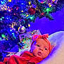 baby, infant, red_clothing, headband, bow, blanket, christmas_tree, christmas_lights, ornaments, presents, holiday, festive, decorations, indoors, soft_texture, cute, portrait, colorful, celebration, cozy