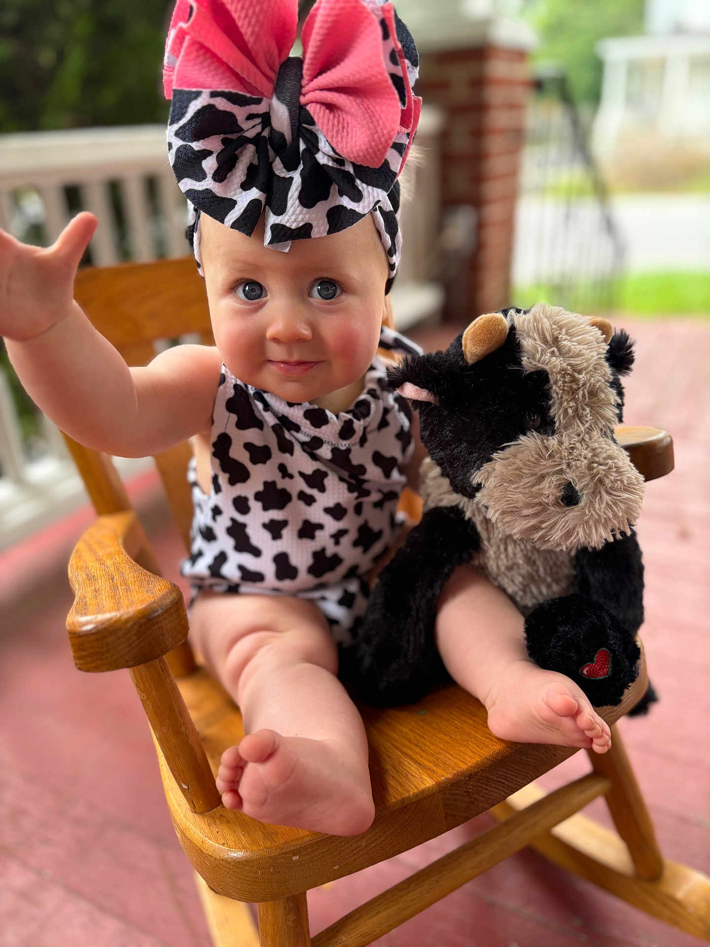Raelynn joined the competition — help win amazing prizes! baby, child, infant, headband, bow, plush_toy, cow_print, rocking_chair, wooden_chair, porch, smiling, cute, reaching_hand, outdoor, soft_toy, foot, legs, blue_eyes, clothing, person