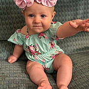 Raelynn is registered to the contest to win money with this photo: baby, child, infant, flower_headband, pink, blue_eyes, floral_outfit, couch, sitting, reaching, cute, chubby, skin, portrait, indoors, happy, childhood, fashion, headwear, playful