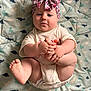 Raelynn is registered to the contest to win money with this photo: baby, infant, child, headband, bow, foot, hand, dinosaur_pattern, quilt, blanket, cute, playful, clothing, onesie, skin, face, expression, lying_down, indoors, soft_lighting