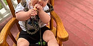 Raelynn joined the competition — help win amazing prizes! baby, child, headband, bow, wooden_chair, porch, red_floor, white_railings, chewing, curious, clothing, shorts, tshirt, hand, foot, face, person, natural_light, indoors, seat