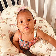 Janiyah is registered to the contest to win money with this photo: baby, child, infant, portrait, sitting, bow, pink_bow, floral_outfit, dress, smiling, wide_eyed, face, eyes, nursery, crib, cushion, teddy_bears, blanket, indoor, close_up