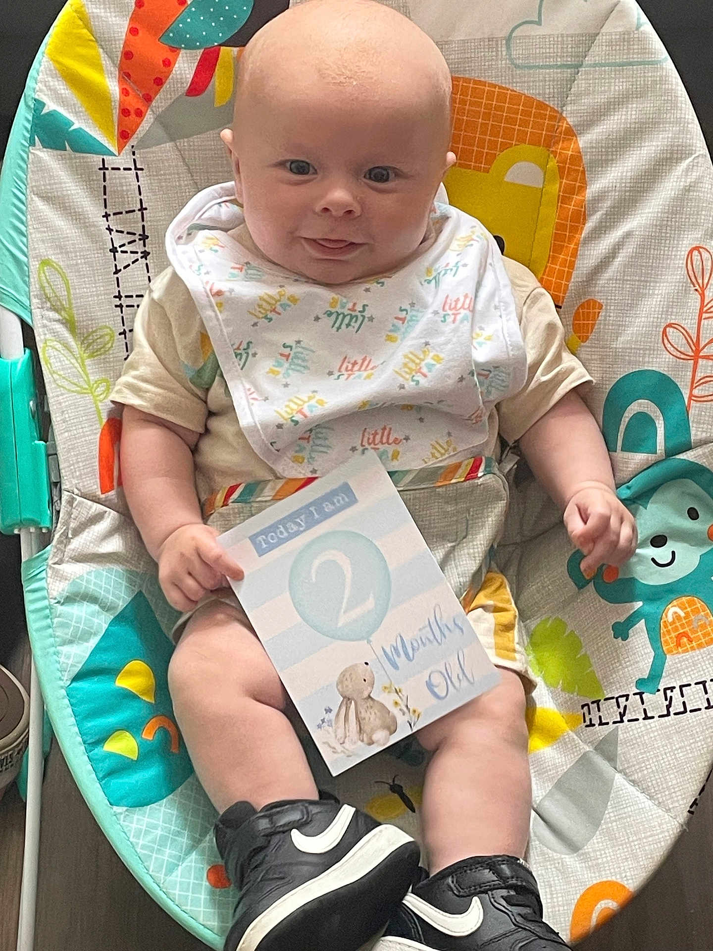 Damien joined the competition — help win amazing prizes! baby, infant, bouncer, bib, sign, shoe, nike, sneaker, colorful, pattern, monkey, smiling, tongue_out, cute, child, playful, clothing, indoor, person, seat