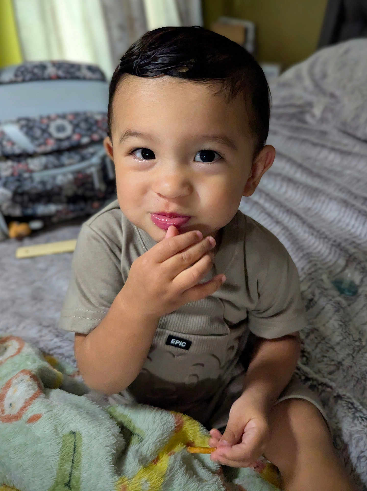 Lorenzo is registered to the contest to win money with this photo: toddler, child, face, hand, snack, blanket, bed, indoor, cute, smile, curly_hair, clothing, person, portrait, comfort, young_child, skin, expression, sitting, cozy
