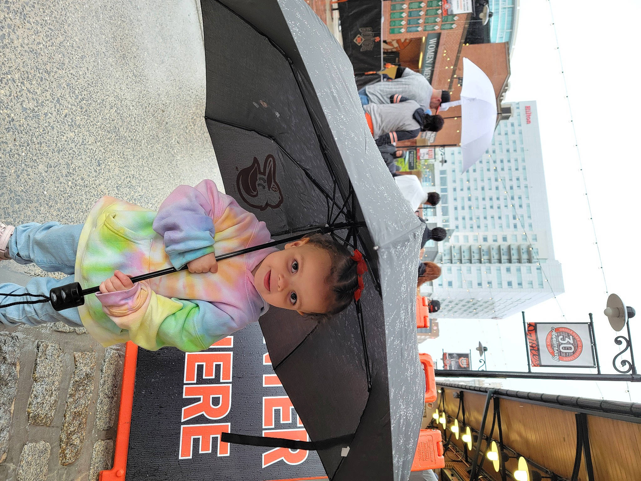 Jackelynn is registered to the contest to win money with this photo: advertising, building, city, event, fashion_accessory, fun, leisure, pedestrian, person, public_event, recreation, sky, street, t_shirt, toddler, tower, tower_block, transport