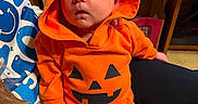 Jameson joined the competition — help win amazing prizes! baby, infant, sleeping, orange_hoodie, pumpkin_costume, costume, hood, person, indoor, lap, clothing, cute, child, resting, face, head, hands, legs, cozy, casual