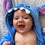 baby, blue_hoodie, purple_ears, smiling, happy, infant, cute, child, face, mouth_open, hand, soft_fabric, teeth_detail, hood, skin, lying_down, indoors, closeup, person, playful