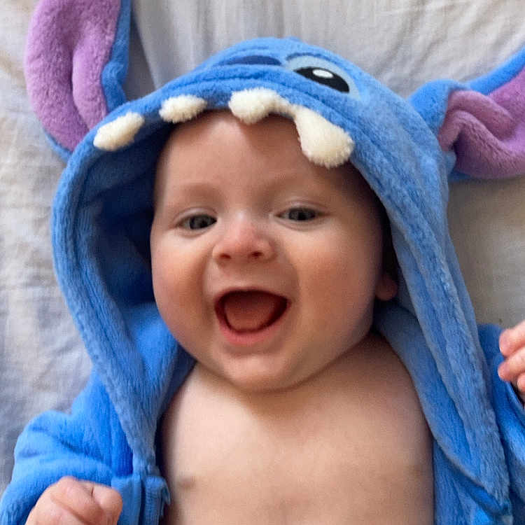 Raphaël Bouthors a rejoint le concours — aidez-le/la à gagner de superbes lots ! baby, blue_hoodie, child, closeup, cute, face, hand, happy, hood, indoors, infant, lying_down, mouth_open, person, playful, purple_ears, skin, smiling, soft_fabric, teeth_detail