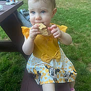Lilianna joined the competition — help win amazing prizes! toddler, child, girl, yellow_dress, minnie_mouse, cracker, snack, outdoor, grass, picnic_bench, pink_shoes, socks, summer, daytime, cute, food, eating, person, park, playground