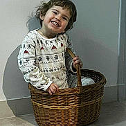 Rafaël a rejoint le concours — aidez-le/la à gagner de superbes lots ! basket, child, cozy, floor, hair, hands, happy, home, indoor, patterned_clothing, playful, portrait, shadow, sitting, smiling, sweater, teeth, toddler, wall, wicker_basket