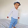 toddler, child, hat, fedora, white_shirt, polka_dots, blue_pants, barefoot, bed, bed_sheet, patterned_sheet, indoor, standing, portrait, person, cute, fashion, confident, smile, young_child