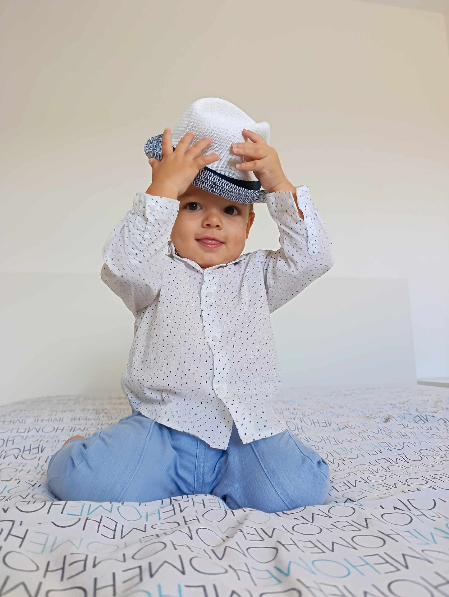 Pablo participe au concours pour gagner de l'argent avec cette photo : toddler, child, hat, bed, shirt, blue_pants, smile, indoor, patterned_bedspread, kneeling, playful, cute, happy, face, hands, young_child, casual_clothing, home, portrait, light_background