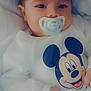 baby, pacifier, mickey_mouse, onesie, infant, blanket, clothing, cute, face, hand, child, portrait, sleepwear, soft, comfort, lying_down, young_child, resting, indoors, adorable