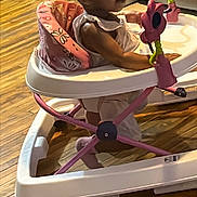 Ezara is registered to the contest to win money with this photo: baby, child, clothing, curious, floor, furniture, hair, home, indoor, person, pigtails, pink, play, seat, toddler, toy, walker, white, wooden_floor, young_child