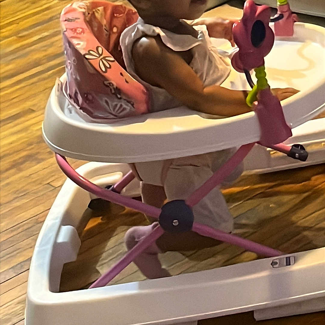 Ezara is registered to the contest to win money with this photo: baby, child, clothing, curious, floor, furniture, hair, home, indoor, person, pigtails, pink, play, seat, toddler, toy, walker, white, wooden_floor, young_child