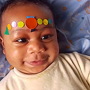 Kyran participe au concours pour gagner de l'argent avec cette photo : baby, smiling, face, child, colorful_stickers, forehead, blanket, patterned, lying_down, cute, infant, happy, indoors, closeup, head, eyes, drool, soft_lighting, clothing, portrait