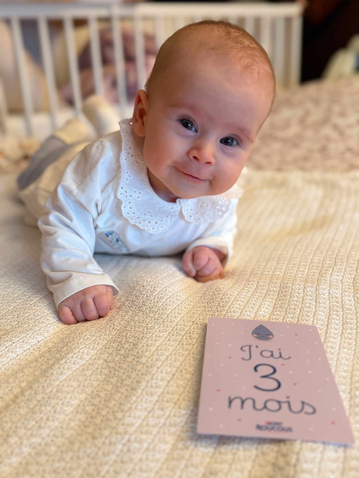 Helena participe au concours pour gagner de l'argent avec cette photo : baby, infant, child, white_clothing, lace_collar, blanket, knitted, bed, milestone_card, age_card, smile, face, eyes, hands, cute, portrait, indoors, soft_light, close_up, lying_down