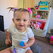 Brynlee is registered to the contest to win money with this photo: toddler, child, smiling, white_onesie, hair_bows, blue_ball, purple_container, toys, stuffed_animals, pampers_box, carpet, sitting, indoor, playroom, cute, happy, person, young_child, home, fun