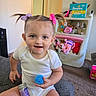 toddler, child, smiling, white_onesie, hair_bows, blue_ball, purple_container, toys, stuffed_animals, pampers_box, carpet, sitting, indoor, playroom, cute, happy, person, young_child, home, fun
