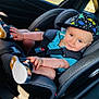 toddler, child, car_seat, blue_shirt, sandals, hat, dinosaur_pattern, car_interior, seatbelt, smile, baby, sunlight, playful, sitting, comfort, window, face, footwear, hand, casual