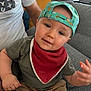 Ethan participe au concours pour gagner de l'argent avec cette photo : toddler, child, cap, red_bib, green_shirt, shorts, couch, adult, living_room, furniture, person, seated, home, cute, indoors, smiling, face, hand, casual_clothing, giraffe_print