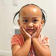 Juminah is registered to the contest to win money with this photo: child, toddler, portrait, smiling, happy, face, eyes, hair, pigtails, hands, cheeks, pink_shirt, clothing, indoors, home, wall, close_up, cute, sitting, photography