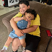 Braylon joined the competition — help win amazing prizes! child, children, hug, smile, couch, denim_overalls, yellow_shirt, carpet, indoor, home, phone, happy, family, sibling, furniture, curly_hair, shorts, socks, footwear, table