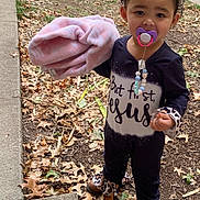 Nevayla is registered to the contest to win money with this photo: toddler, child, pacifier, blanket, outdoor, grass, leaves, sidewalk, curly_hair, bow, boots, black_clothing, patterned_clothing, fall, nature, young_child, person, standing, cute, curious